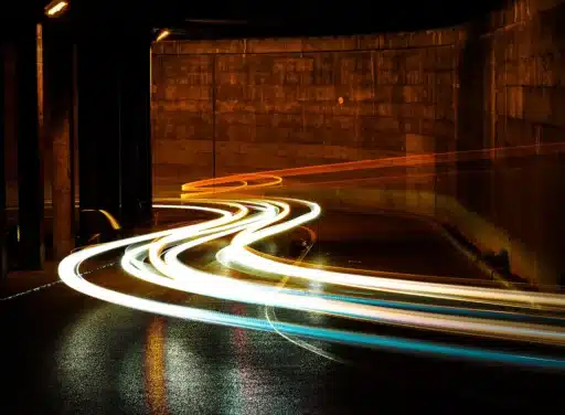 Long-exposure shot of cars going through a tunnel at night has their lights leave long trails