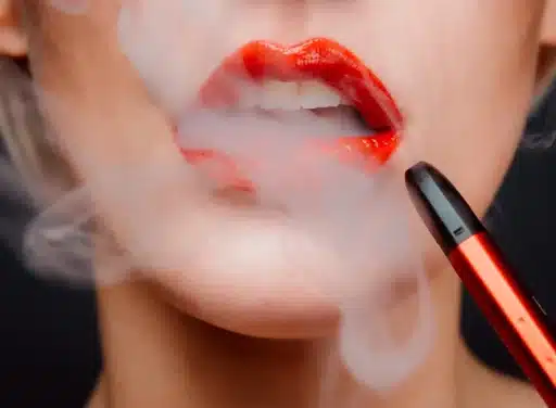 Closeup photo of a woman's mouth and painted lips getting smoke from her vape everywhere