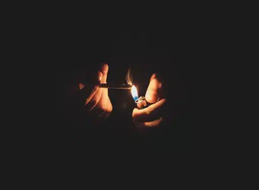 Male hands emerge from the darkness to light a cigarette