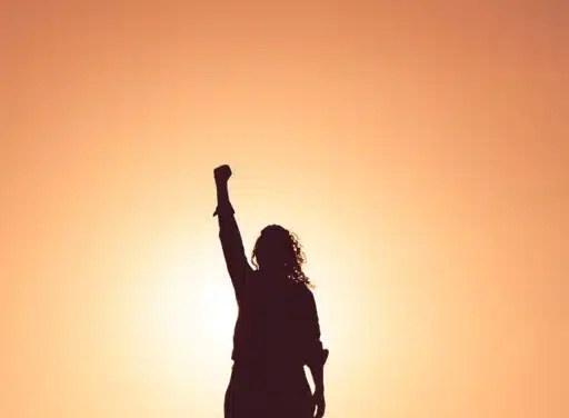 Woman backlit by the sun during sunset raises her fist