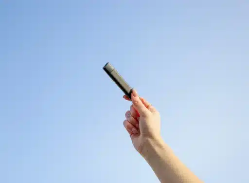 Female hand holds a black vape device to the sky