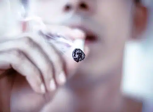 Closeup of man putting a smoking cigarette to his mouth