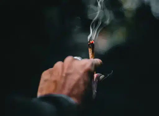 Male hand holding a blunt with smoke rising