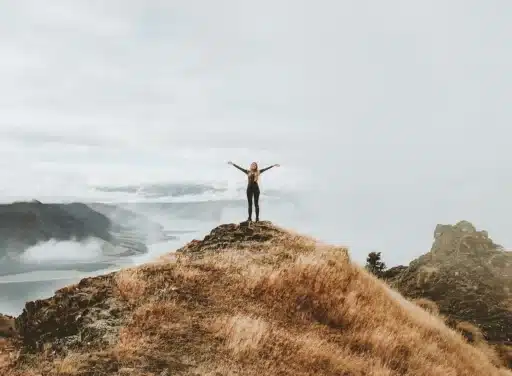 Woman standing on top of hill with arms raised